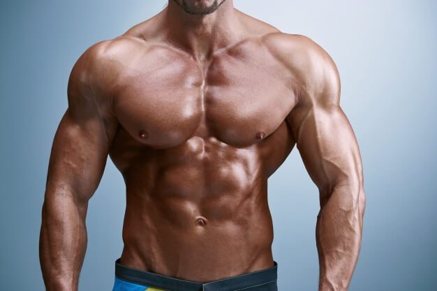 Torso of a tanned, muscular male bodybuilder with defined abs and chest, representing a lean physique.